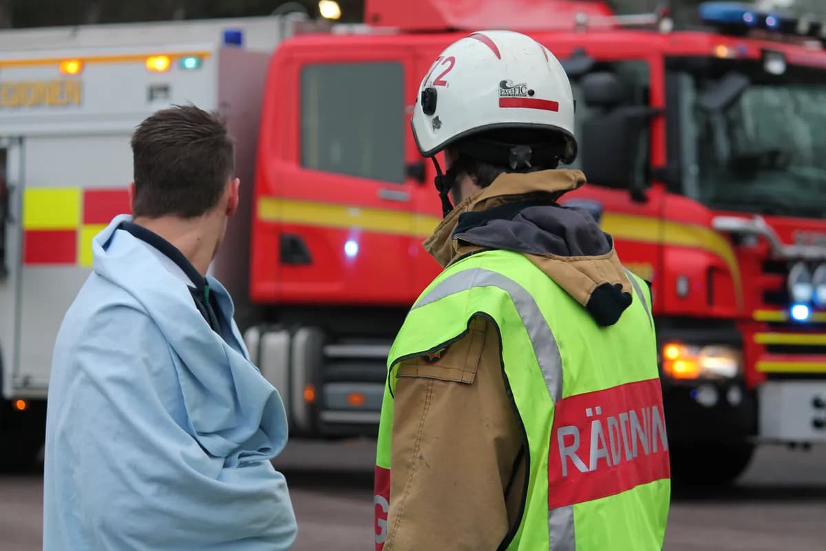Firefighter in high-vis vest next to affected person at accident scene with fire truck behind
